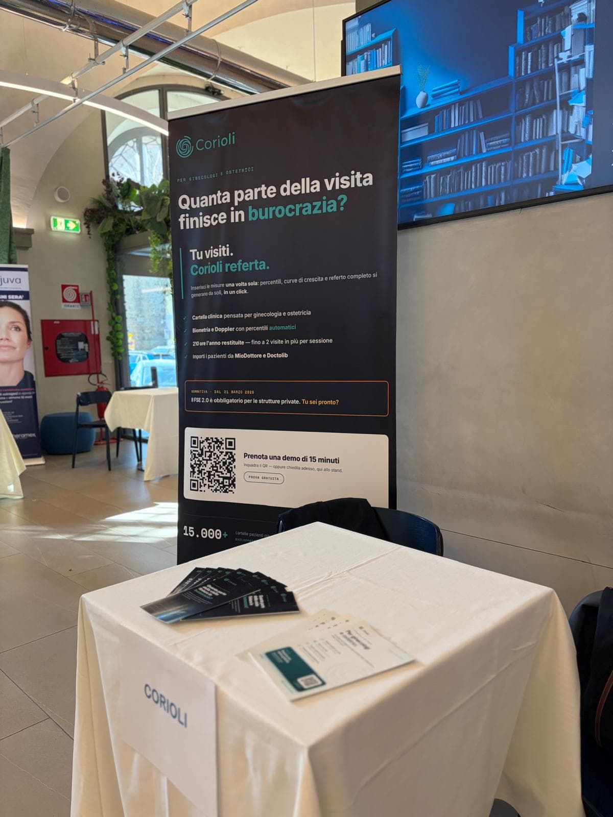 Lo stand Corioli al congresso sui miomi uterini, con il roll-up 'Tu visiti. Corioli referta.' e il tavolo con le brochure.